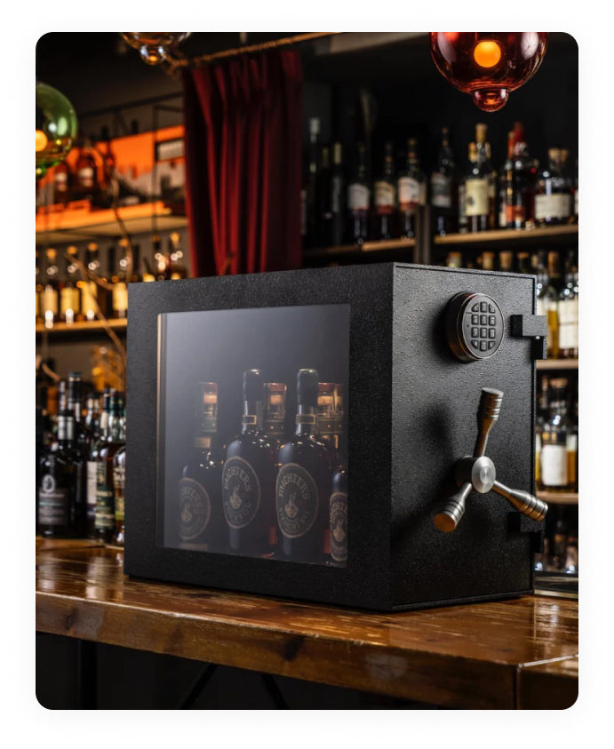 The Mini Vault is your ultimate sanctuary for prized spirits collections. Crafted with spirits enthusiasts in mind, this Mini Vault offers secure and stylish storage for 10-15 bottles of your finest spirits. The robust steel plate construction ensures durability and security, allowing you to rest easy knowing your valuable bottles are safe from unwanted access.
<br /><br />
  Designed to blend seamlessly into your space, the Mini Vault fits neatly on countertops or standalone bars, making it a convenient addition to any setting. The distinctive machined aluminum tri-spoke handle adds a touch of sophistication while providing easy access to your curated collection. The UL-certified La Gard Electronic Lock, paired with a bulletproof 19mm glass window, ensures both security and an impressive display of your spirits assortment, all while keeping it protected from unintended opening.
<br /><br />
  With its patented design and individually numbered for authenticity, the Mini Vault stands out as a piece of functional art. For those seeking a personal touch, custom airbrushed artwork on the inside of the door is available for an additional cost.
<br /><br />
  Whether you're a whiskey connoisseur or a business owner in the hospitality industry, this handcrafted masterpiece offers the perfect blend of security, style, and peace of mind. Elevate your personal bar experience - choose the Mini Vault, where craftsmanship meets security.